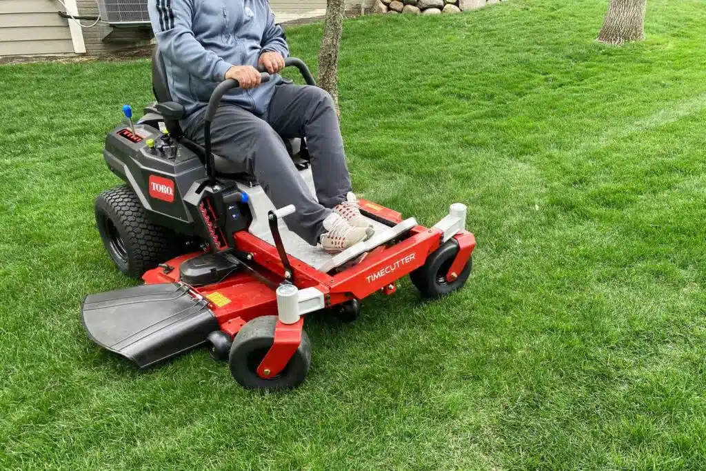Man riding red Toro lawnmower in green yard
